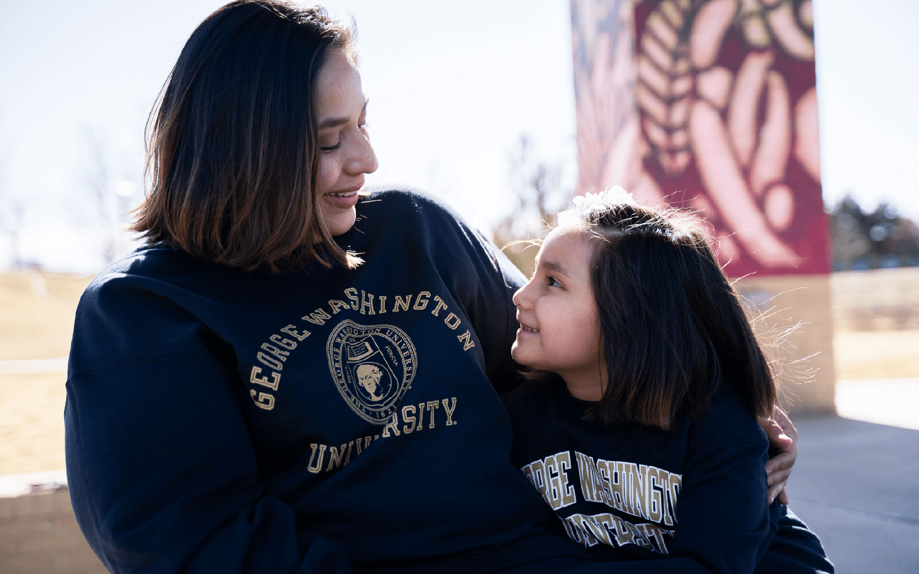 Erica Gonzalez, wearing a George Washington University sweatshirt, smiles down at her daughter as they talk together.