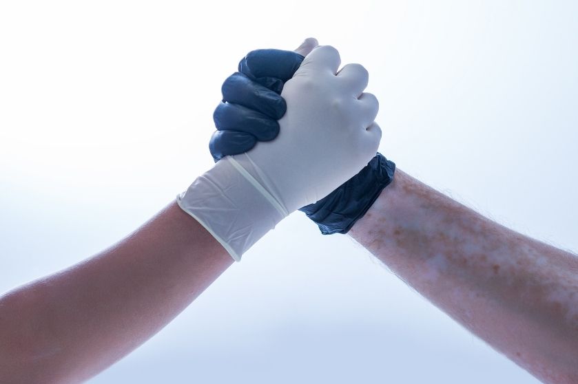 two peoples hands covered by gloves making a fist together
